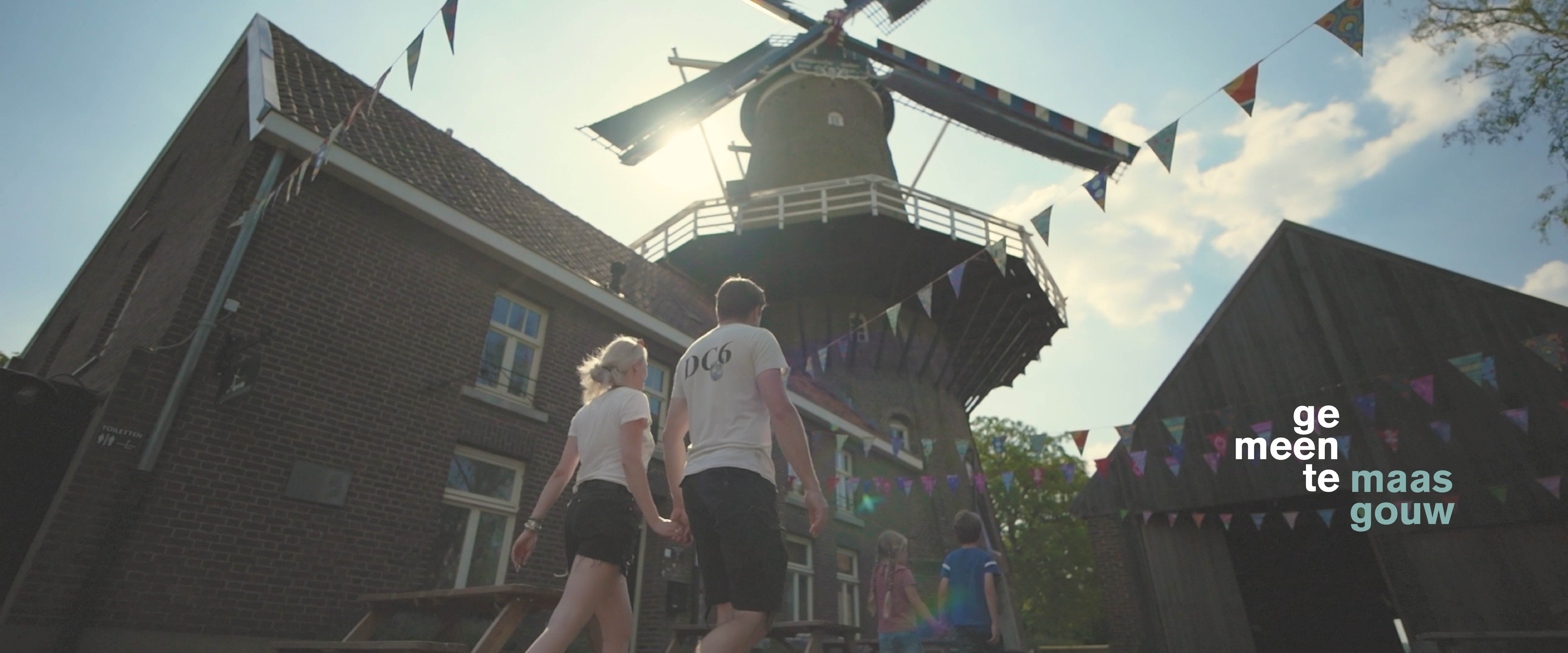 Man en vrouw wandelen hand in hand voorbij de Hompesche Molen gezien vanuit kikkerperspectief waarin de zon door de wieken van de molen schijnt.
