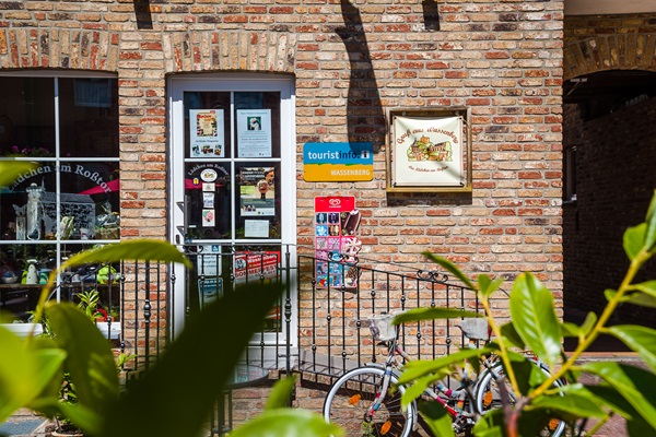 Entrance to the tourist information point in Wassenberg, with brochure rack, signs and bikes in front.