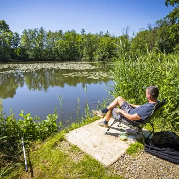 Man zit ontspannen aan een visstek aan een vijver, omringd door natuur tijdens het vissen in Limburg.