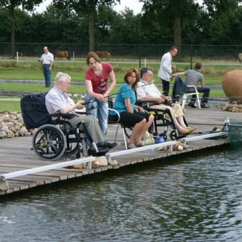 Bezoekers, waaronder mensen in een rolstoel, vissen vanaf een steiger bij Forelrivier in Reuver.
